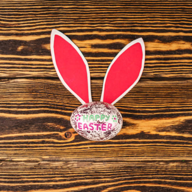 istock Shiny Easter egg with paper rabbit ears on wooden background. Top view 1304304820