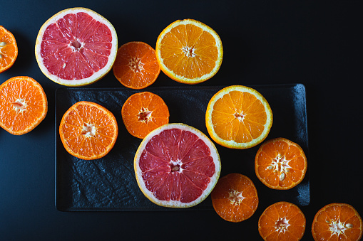 Citrus fruit on dark plate and black background, flat lat, from above.