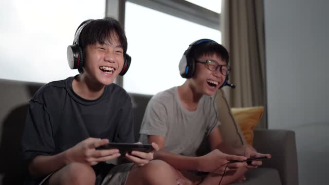 2 Asian Chinese sibling brother sitting on sofa playing video game in living room