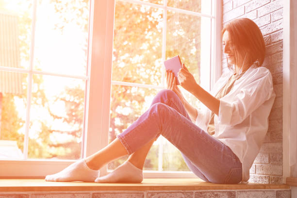 istock Young woman sitting at windowsill. Working on tablet. Online study concept. 1304312535
