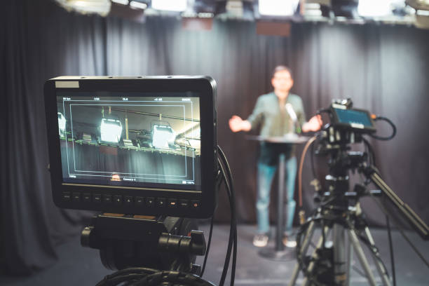 istock Young journalist in a television recording studio is talking into a microphone, blurry film cameras 1304319184