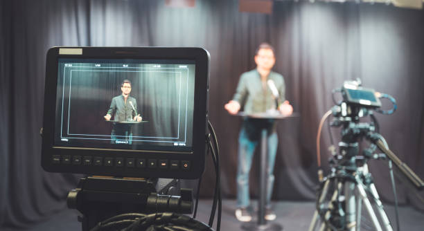 istock Young journalist in a television recording studio is talking into a microphone, blurry film cameras 1304319210