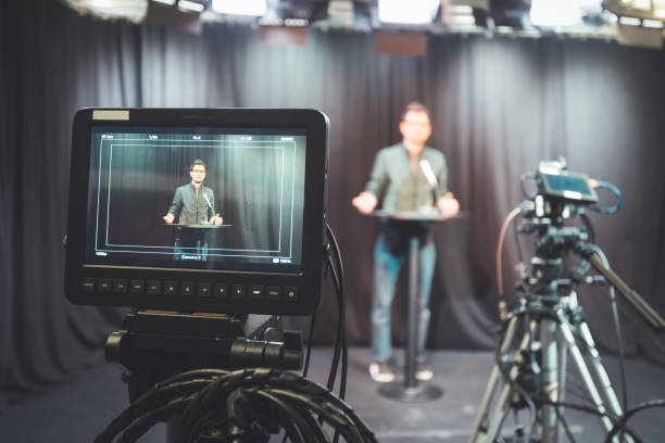istock Young journalist in a television recording studio is talking into a microphone, blurry film cameras 1304319229