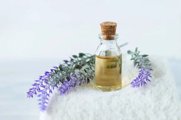Front view of lavender in oil and  lavender flowers on a white towel on marble background.