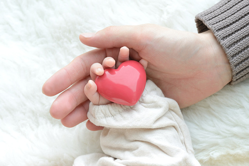 La mano del bebé con objeto cardíaco y la mano de la madre photo