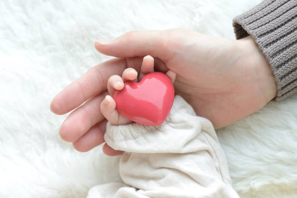Baby's hand with heart object and mother's hand