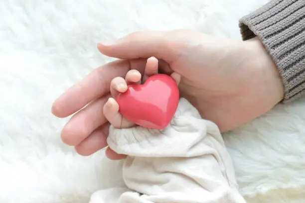 Photo of Baby's hand with heart object and mother's hand