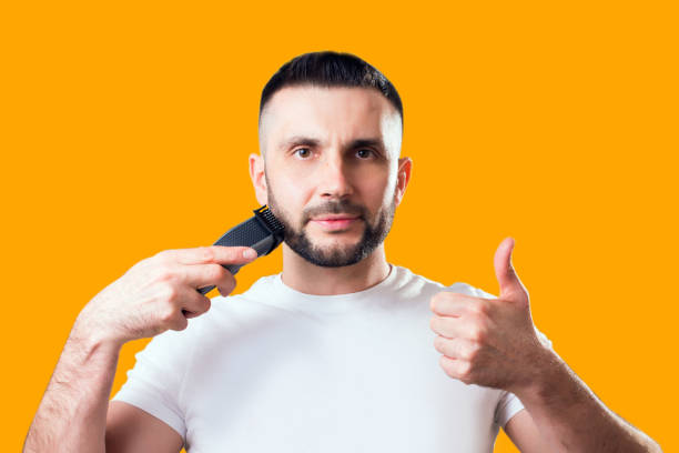 istock Man shaves his beard with a trimmer on a yellow background 1304331444