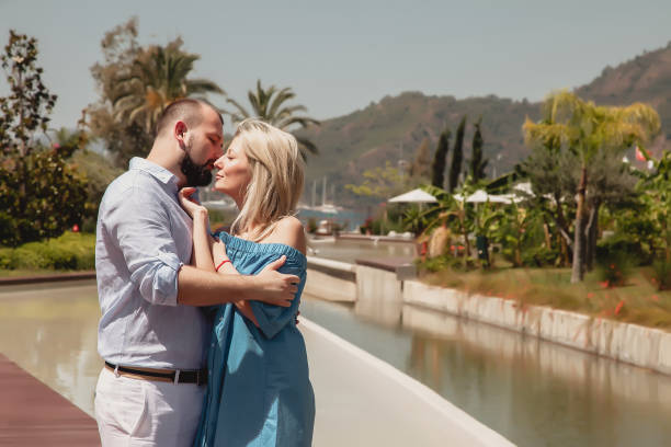 loving couple enjoying honeymoon in luxury hotel, walking through grounds with palm trees and swimming pool - honeymoon beach swimming pool couple imagens e fotografias de stock