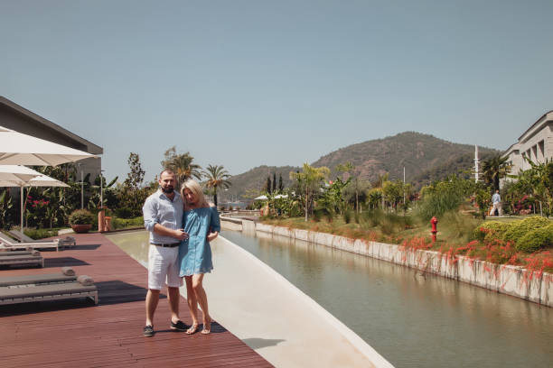 loving couple enjoying honeymoon in luxury hotel, walking through grounds with palm trees and swimming pool - honeymoon beach swimming pool couple imagens e fotografias de stock