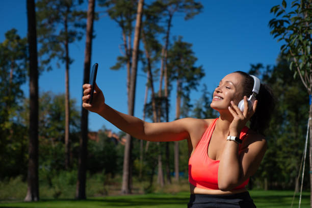 uma mulher feliz com fones de ouvido ouvindo a música e fazendo selfie ao ar livre - distance running audio - fotografias e filmes do acervo