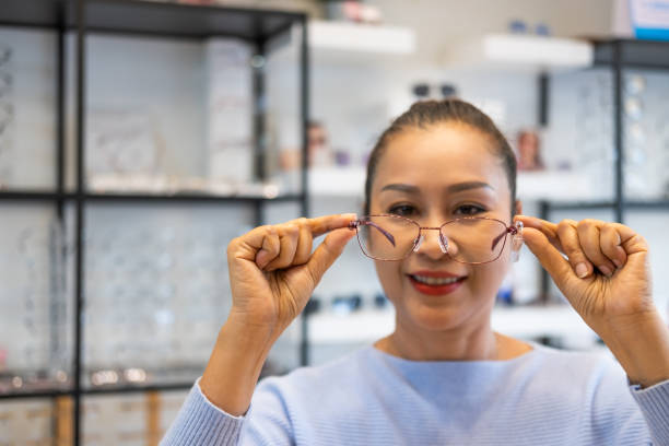 istock Selective focus at glasses. Senior elder Asian women smile and look at the mirror while choosing beautiful glasses frame trial inside of optical shop, store.  Eye sight for elder, healthcare. 1304336035