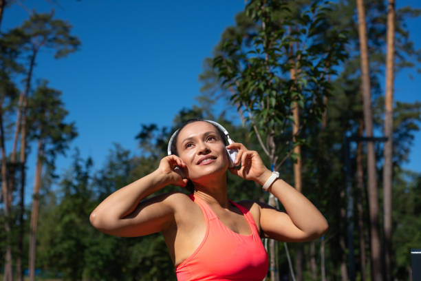 retrato de uma mulher em forma com fones de ouvido em pé em uma floresta de pinheiros e olhando para longe - distance running audio - fotografias e filmes do acervo