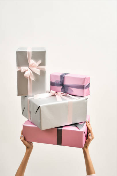 istock Holidays and celebration concept. Female hands holding stack of wrapped colorful gift boxes over the head against light background, vertical shot 1304339443
