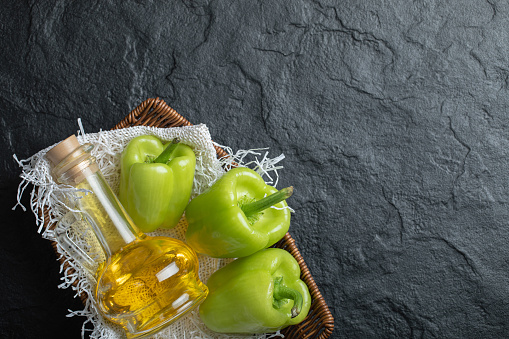 Top view of pile of green peppers with olive bottle in basket over black background. High quality photo