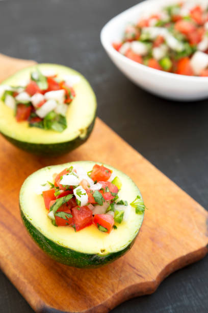 istock Homemade Pico de Gallo Stuffed Avocado on a rustic wooden board on a black surface, side view. 1304343165