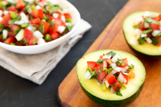 istock Homemade Pico de Gallo Stuffed Avocado on a rustic wooden board on a black surface, low angle view. Close-up. 1304343220