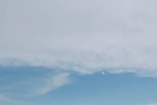 Moon in the sky. Moon with small clouds at dawn, cold and blue tones, moon on the left.