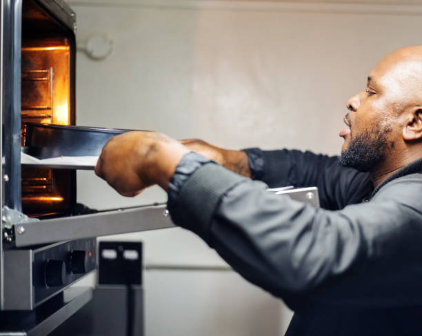 Baker putting cake tins filled with cake mixture into the oven for baking