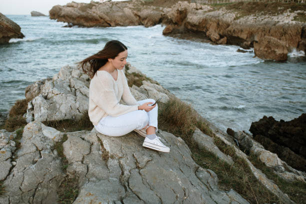 istock Young woman using a smart phone sitting by the sea 1304353149