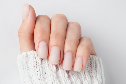 Matt nude nails close up o the light background. Winter manicure, woman hand in the warm sweater.