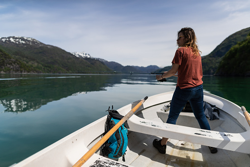 Woman fishing with a rod from a small boat in the sea by a fjord, in Norway