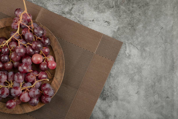 istock Wooden plate of red grapes placed on marble surface 1304359781