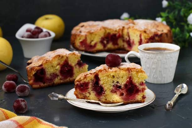 istock Berry pie with cherries is located on a plate on a dark background. In the foreground is a piece of cake and a cup of coffee 1304363045