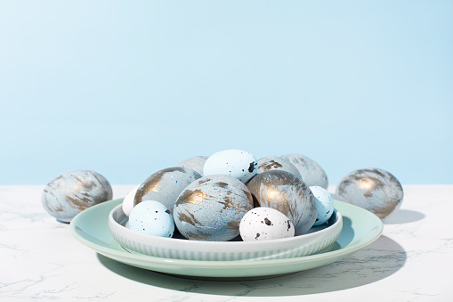 Festive Easter holiday greeting card background. Easter blue golden eggs, quail eggs, tree branch on gray marble table. Copy space, selective focus, hard shadows.