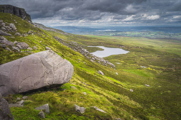 istock Large boulder and rubble on Cuilcagh Mountain mountainside, small lake in valley below 1304369913