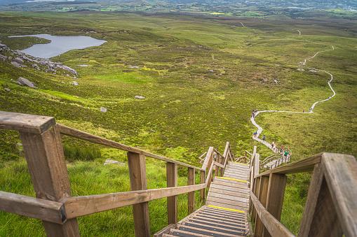 Top view on people climbing on steep steps and stairs of wooden boardwalk, to reach Cuilcagh Mountain peak, Northern Ireland