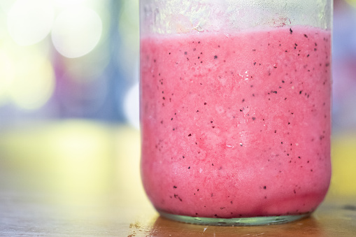 Strawberry smoothie in big jar glass, close up on wood table.