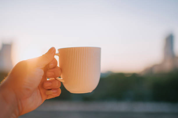 human hand holding coffee cup backlist sunrise