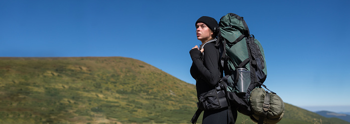 close-up portrait of a young woman tourist with a large backpack. against the background of the mountains. Back view. Baner. Copy space