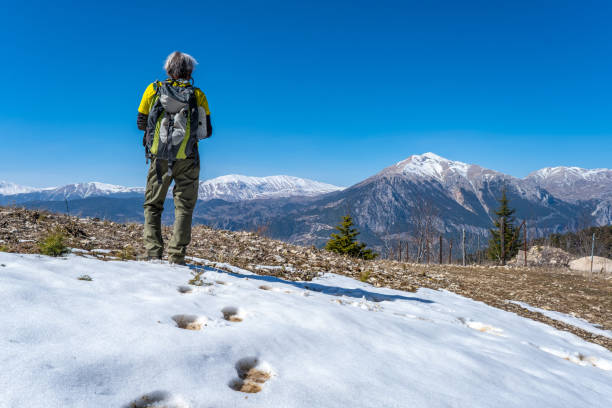 Footprints in the open-air snow. A 60-year-old man with a backpacking hiker in the continuation of his footprints. Snowy mountain range landscape