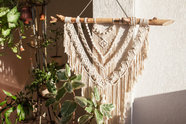istock Handmade macrame  100% cotton wall hanging with green leafes on a white wall.  Modern eco macrame decoration with wooden stick in the interior. Bright solar light 1304381129