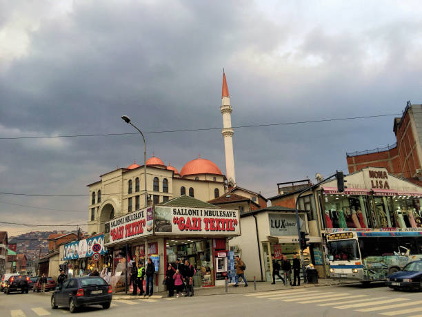 Cars driving through the old town of Pristina in Kosovo under an overcast sky and pedestrians walking along the street with a mosque in the background March 24,2016