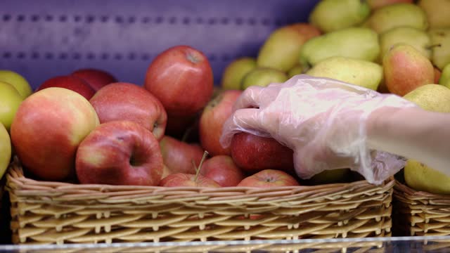 Female hand in glove picks fruits apples from basket in supermarket