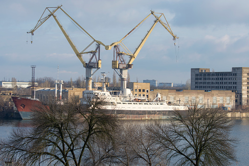 Mykolaiv, Ukraine - January 31, 2021: View of the shipyard in the morning. Two tower cranes and a ship hull.