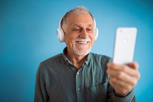 Senior man holds mobile phone and listening music on headphone