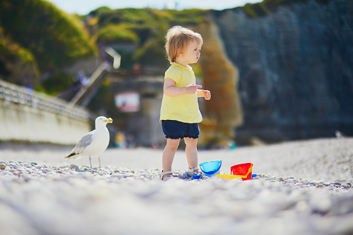 Adorable toddler girl playing with pebbles on the beach in Etretat, Normandy, France. Child having fun near the sea. Outdoor activities for kids