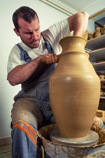 Young potter making vase on pottery wheel in his workshop.