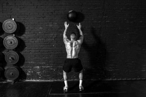 istock Young active strong sweaty focused fit muscular man with big muscles doing throwing medicine ball up on the wall for cross training hard core workout in the gym real people exercise 1304396805