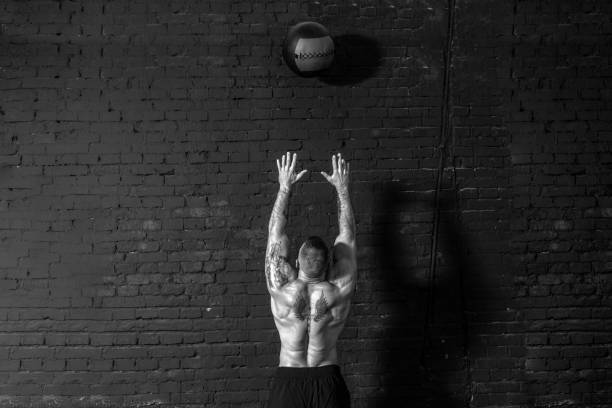 istock Young active strong sweaty focused fit muscular man with big muscles doing throwing medicine ball up on the wall for cross training hard core workout in the gym real people exercise 1304396811