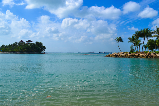 Tropical island landscape, turquoise ocean, blue sky with white clouds on sunny summer day. Sentosa island, Singapore. Travel blog design. Background for relaxing vacation