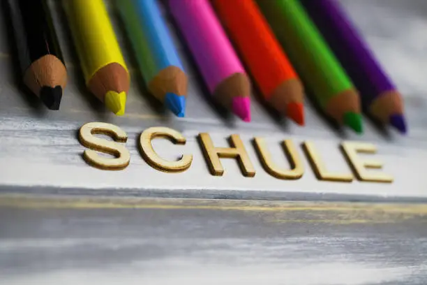 Closeup of row multi colored crayons on wood table with german word schule (english meaning: school)