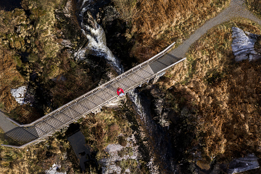 The view from a drone of a senior man standing alone on a footbridge looking at his map the location is Dumfries and Galloway south west Scotland