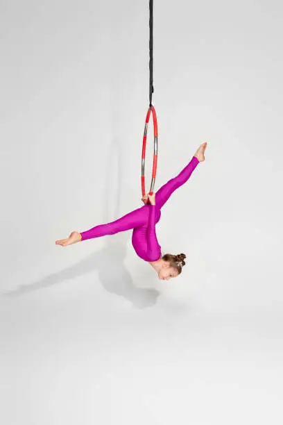 little child girl gymnast in pink sportwear doing twine on an aerial hoop