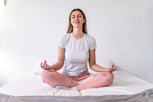 Young woman meditating in the bedroom in the morning.