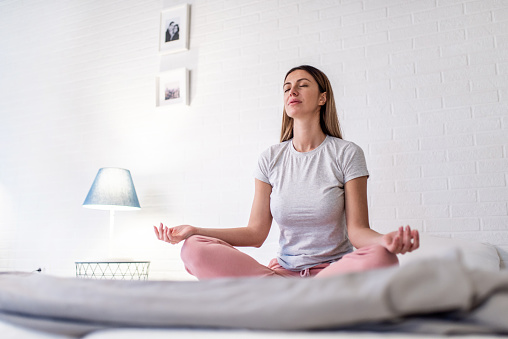 Young woman meditating in the bedroom in the morning.